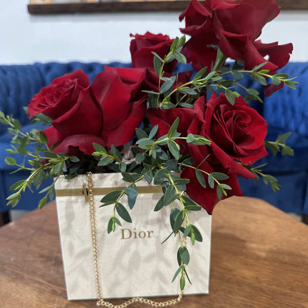 Red roses arranged in a white Dior gift bag with greenery.