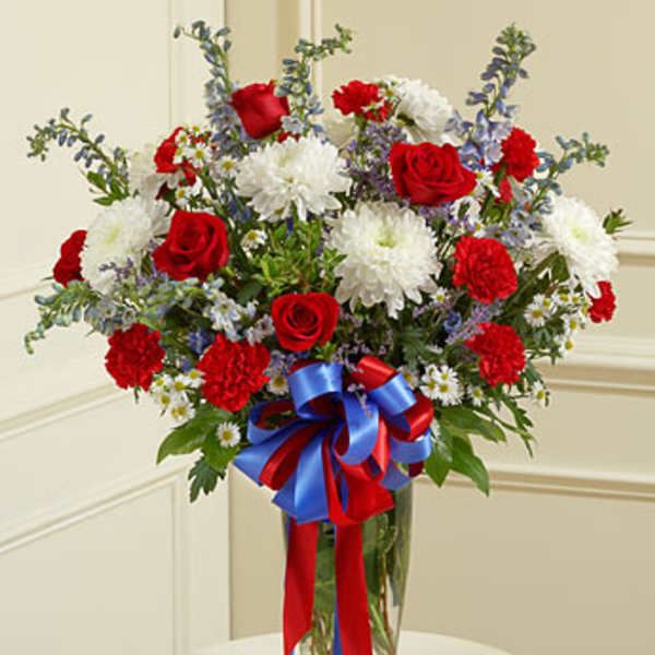 Red roses and white chrysanthemums in a glass vase with a red and blue ribbon