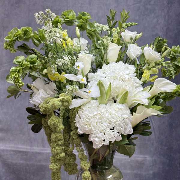 White flowers and green accents arranged in a clear glass vase