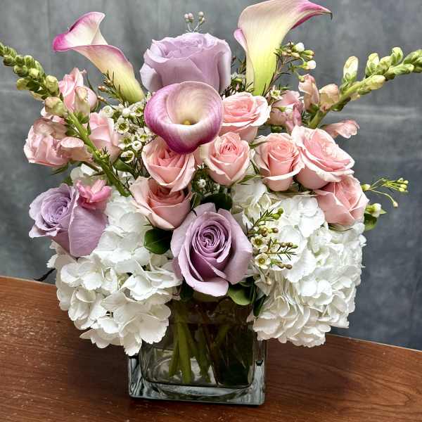 Pink roses and white hydrangeas in a square glass vase with calla lilies