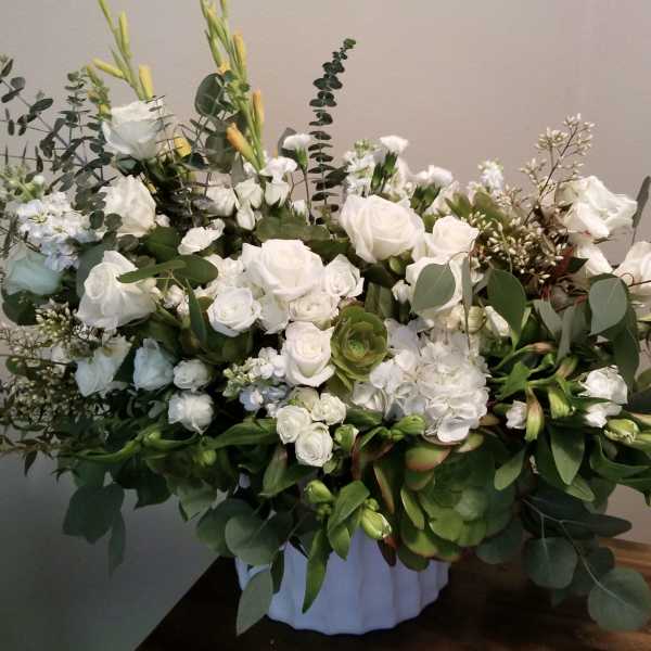 White rose arrangement in a white container with eucalyptus and greenery
