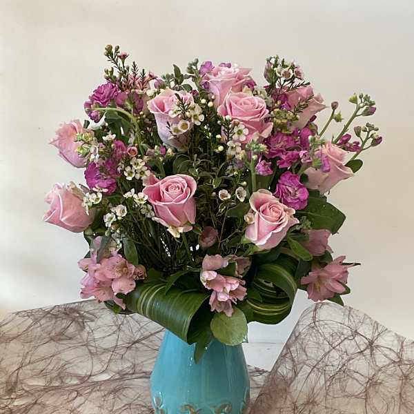 Pink roses and small purple flowers arranged in a turquoise vase