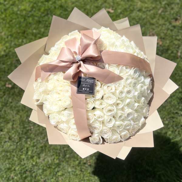 Large bouquet of white roses wrapped in beige paper with a pink ribbon