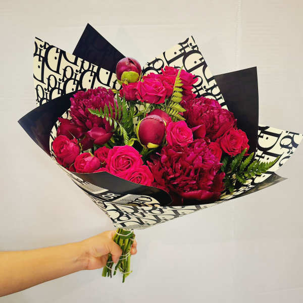 Handheld bouquet of hot pink roses and deep magenta blooms in patterned wrap