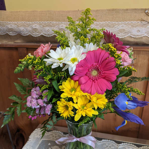 Mixed bouquet in a glass vase with pink, yellow, white, and blue flowers