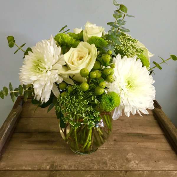 White roses and chrysanthemums in a glass vase with green accents