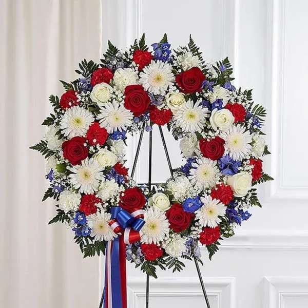 Patriotic red, white, and blue standing wreath with roses, carnations, and daisies on a metal easel