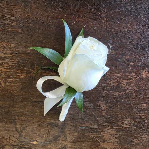 White rose boutonniere with green leaves and a white ribbon