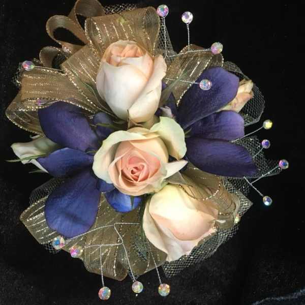 Corsage with pale roses, purple petals, and gold ribbon on black fabric