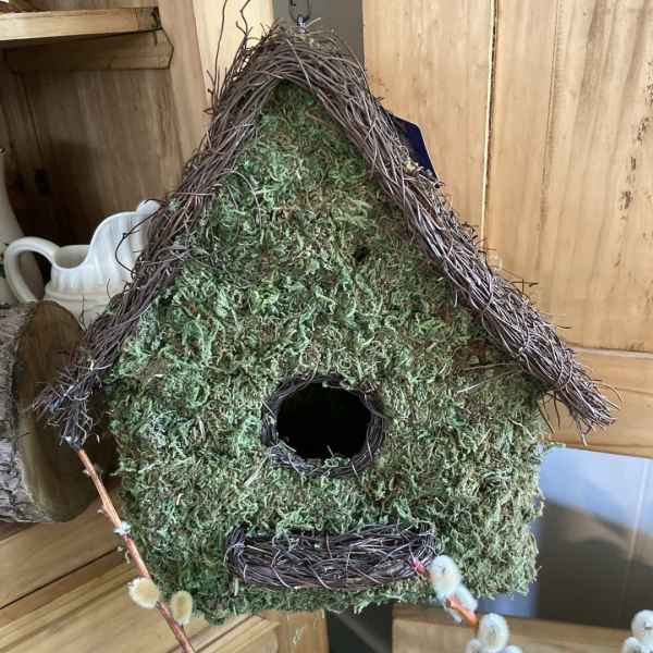 Moss-covered birdhouse with a twig roof and round opening