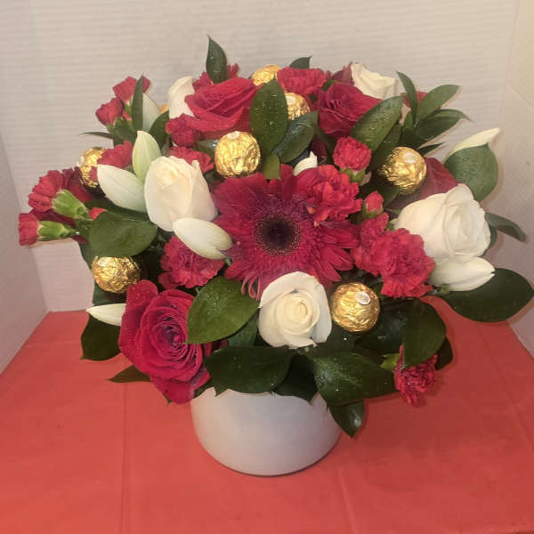 Bouquet of red and white flowers in a white vase with gold chocolates