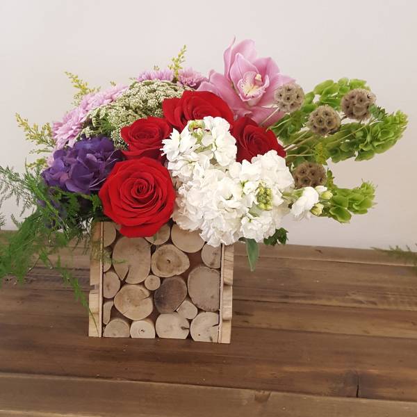 Mixed bouquet of red, white, pink, and purple flowers in a wooden log box