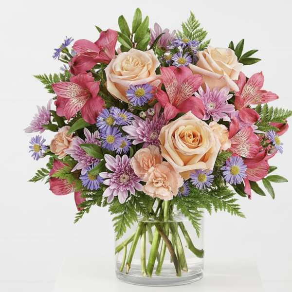 Bouquet of peach roses, pink alstroemeria, and purple daisies in a glass vase