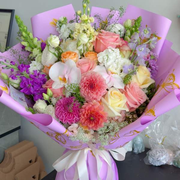 Mixed bouquet of pink, white, and purple flowers wrapped in lavender paper