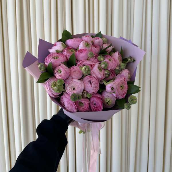 Handheld bouquet of pink ranunculus wrapped in lavender paper