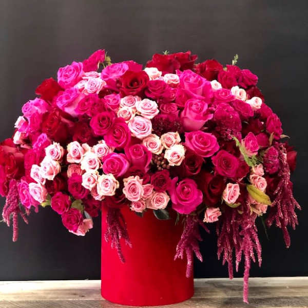 Large arrangement of pink and red roses in a red cylindrical vase