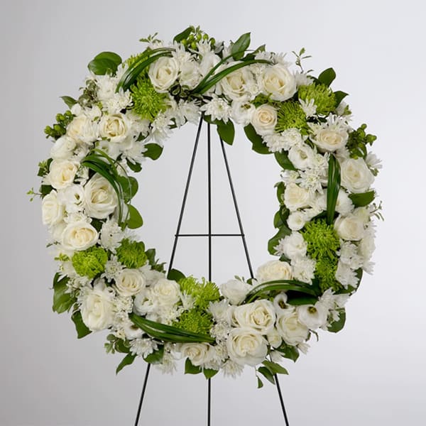 White floral wreath on a black stand with green accents