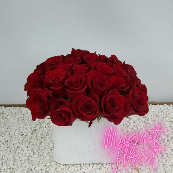 Red roses arranged in a white box with a pink neon sign