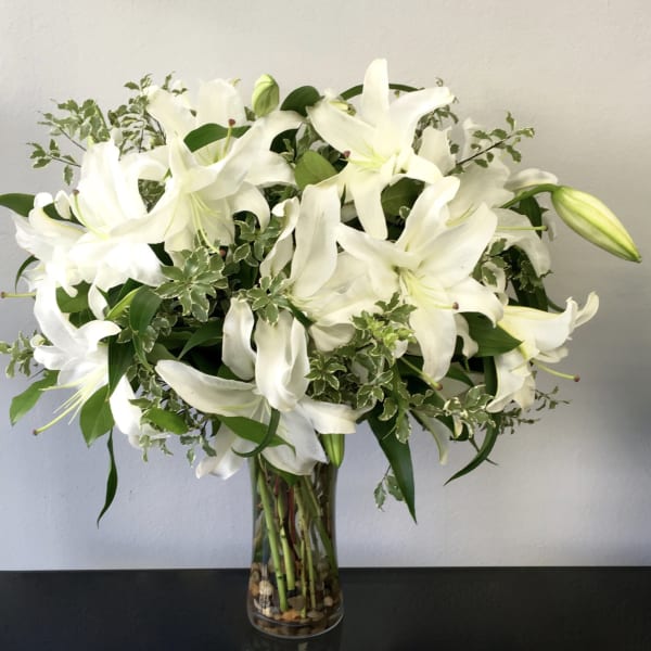 White lilies arranged in a clear glass vase with mixed greenery