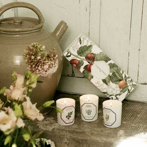 Lit candles beside a ceramic jug and a floral box