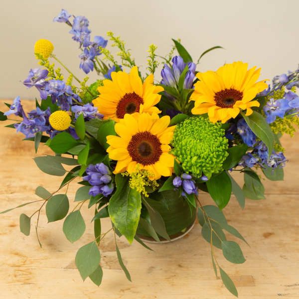 Sunflowers and blue flowers arranged in a low vase