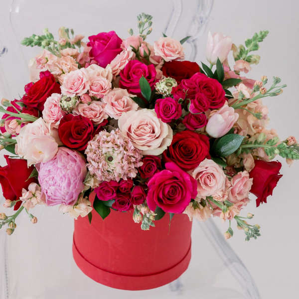 Mixed pink and red roses arranged in a red hat box