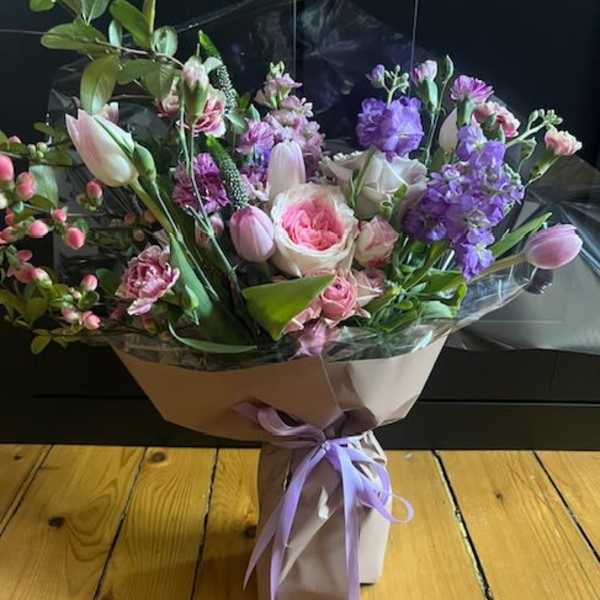 Bouquet of pink and purple flowers wrapped in paper with a lavender ribbon