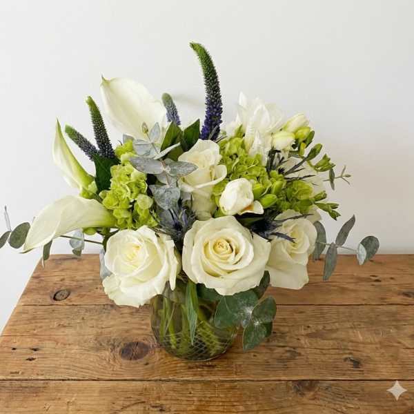White roses and calla lilies in a glass vase with green and purple accents