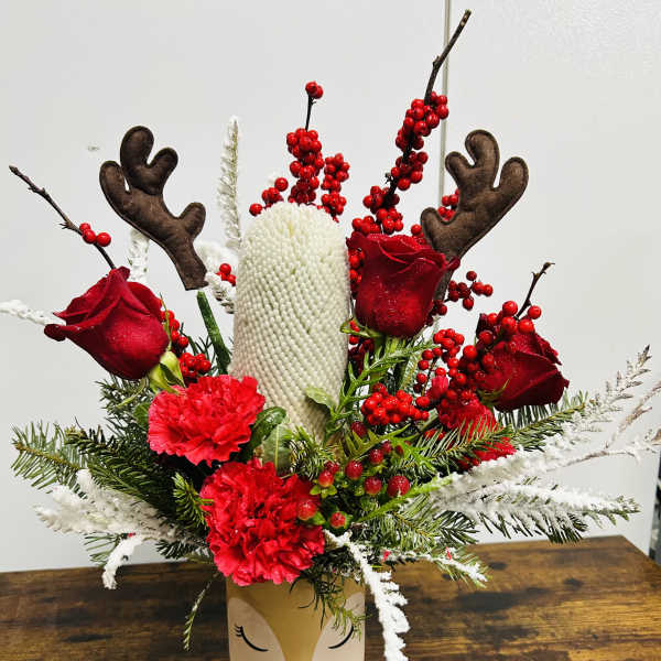 Holiday arrangement with red roses, carnations, and reindeer antlers in a decorative vase
