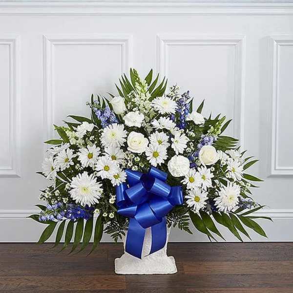 White and blue floral standing spray with a large ribbon on a pedestal.