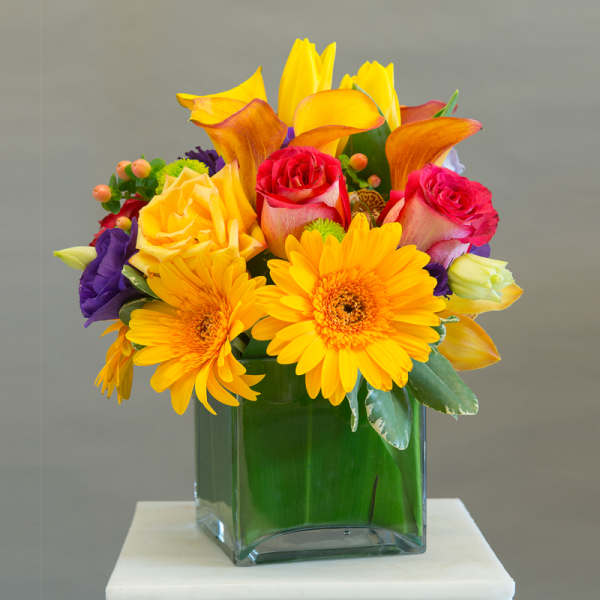 Colorful bouquet of roses, calla lilies, and gerbera daisies in a glass vase