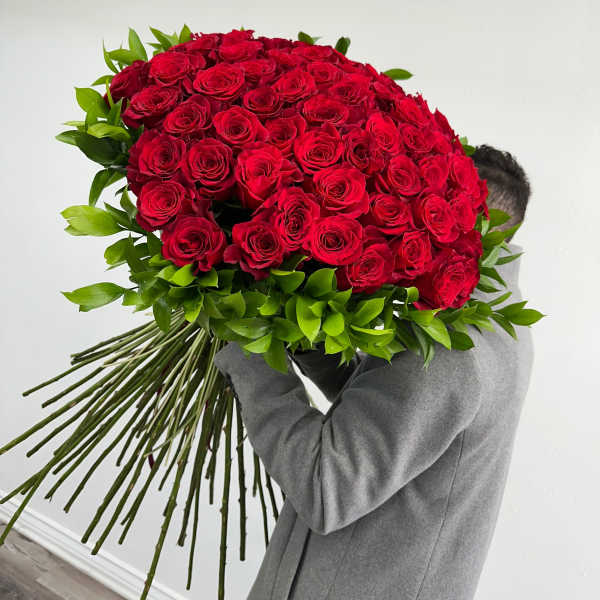 Large bouquet of red roses with green foliage, held by a person