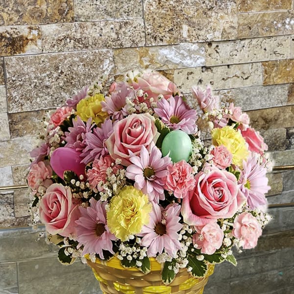 Basket arrangement of pink roses, daisies, and carnations with pastel eggs