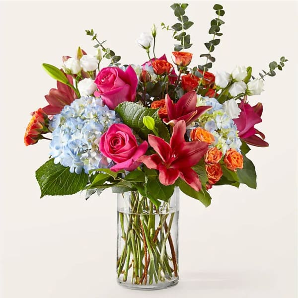 Mixed bouquet of roses, lilies, and hydrangeas in a clear glass vase