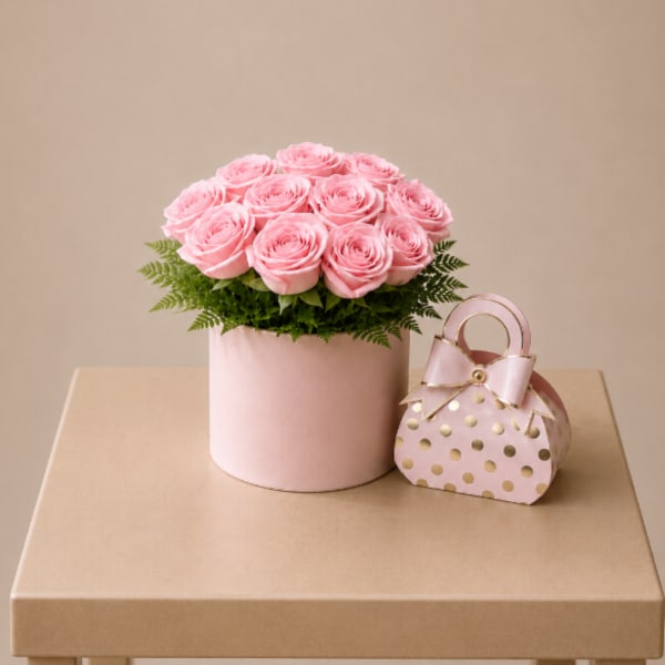 Pink roses in a round box with a small polka-dot gift bag beside it