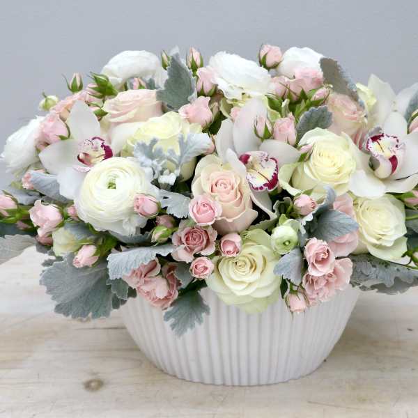Pastel bouquet of roses, orchids, and ranunculus in a white vase