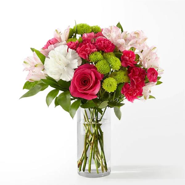 Bright pink roses and carnations with green button mums and white blooms in a clear glass vase.