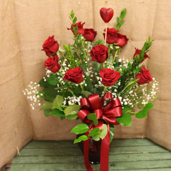 Red roses in a glass vase with a red ribbon and heart pick