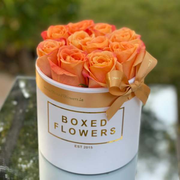 Orange roses arranged in a white round box with a ribbon bow
