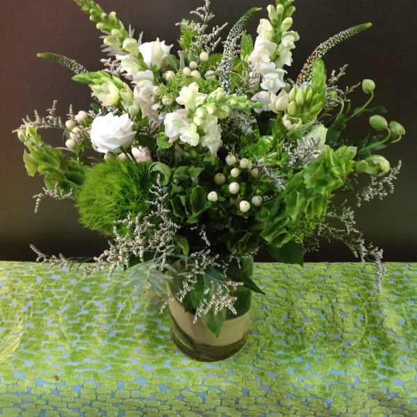 Tall green and white floral arrangement with snapdragons and roses in a clear glass cylinder vase