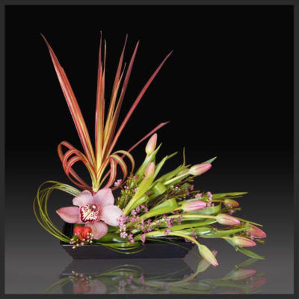 Pink orchid arrangement with long decorative leaves in a low black container