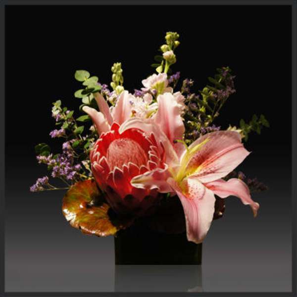 Pink lilies and a red protea in a black vase