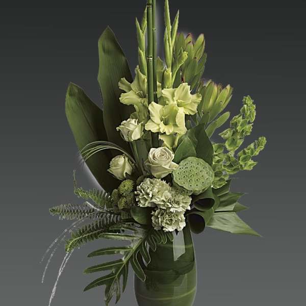 Green floral arrangement in a glass vase with tropical leaves and pale blooms