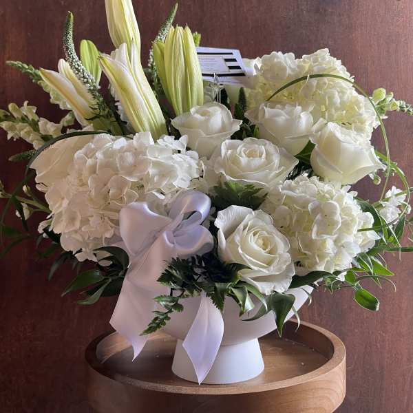 White floral arrangement in a pedestal vase with a lavender ribbon