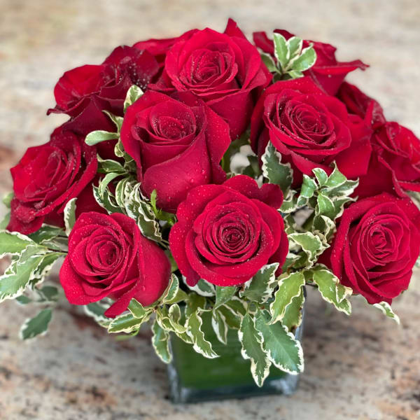 Red roses arranged in a clear glass vase with variegated greenery