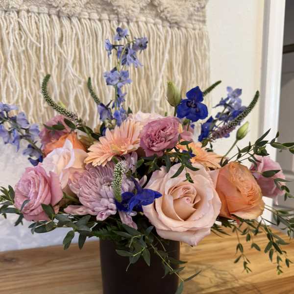 Mixed bouquet of pink and peach roses with blue flowers in a dark vase