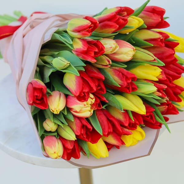 Bouquet of red, yellow, and pink tulips wrapped in pale paper