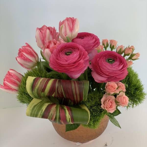 Pink tulips and ranunculus in a round vase with striped leaves