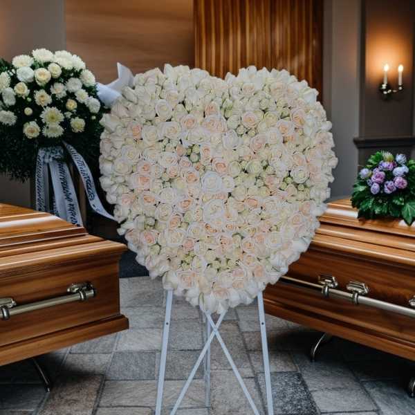 Heart-shaped white rose funeral spray on a stand