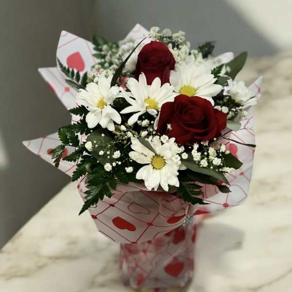 Bouquet of red roses and white daisies in heart-patterned wrap